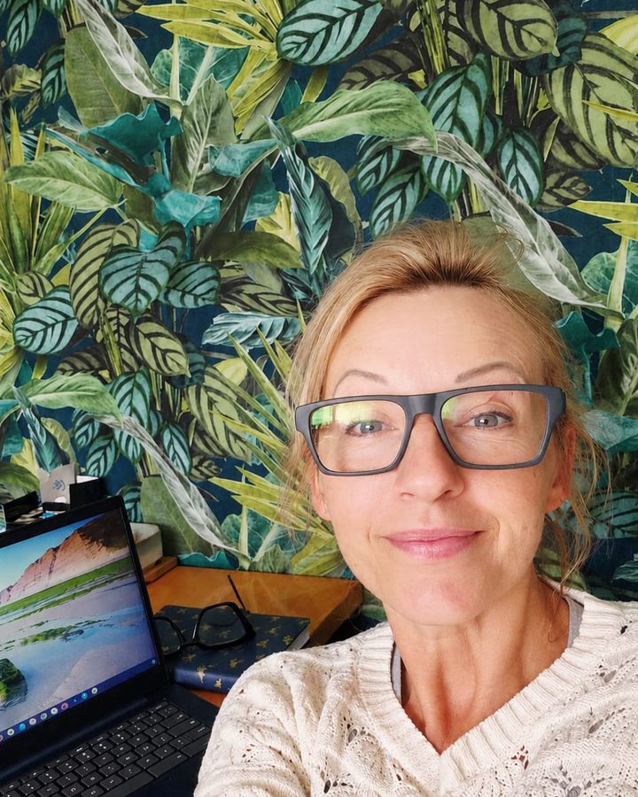 Sylwia, founder of Amber Heart CIC, smiling at the camera in front of a leafy patterned wall