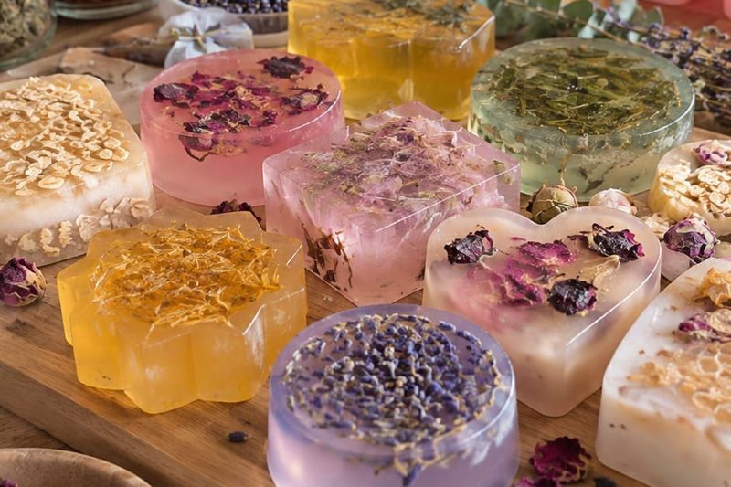 Handmade soaps decorated with dried petals and lavender, laid out on a wooden board among jars of dried flowers and moulds